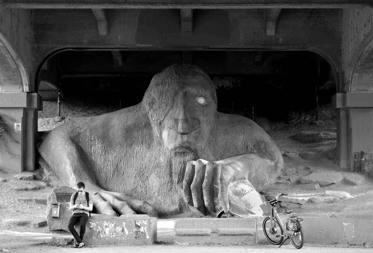 SEATTLE, WA - JUNE 9: (EDITORS NOTE: This image has been converted to black and white) A pedestrian looks on his phone in front of The Fremont Troll (also known as The Troll, or the Troll Under the Bridge) during the 2019 Rock'n'Roll Seattle Marathon and 1/2 Marathon on June 9, 2019 in Seattle, Washington. The Troll, holding an actual Volkswagen bug, is 18ft high and weighs 13,000 lbs, and was sculpted by four local artists Steve Badanes, Will Martin, Donna Walter, and Ross Whitehead out of steel rebar, wire, and concrete. Donald Miralle/Getty Images for Rock'n'Roll Marathon /AFP == FOR NEWSPAPERS, INTERNET, TELCOS & TELEVISION USE ONLY ==