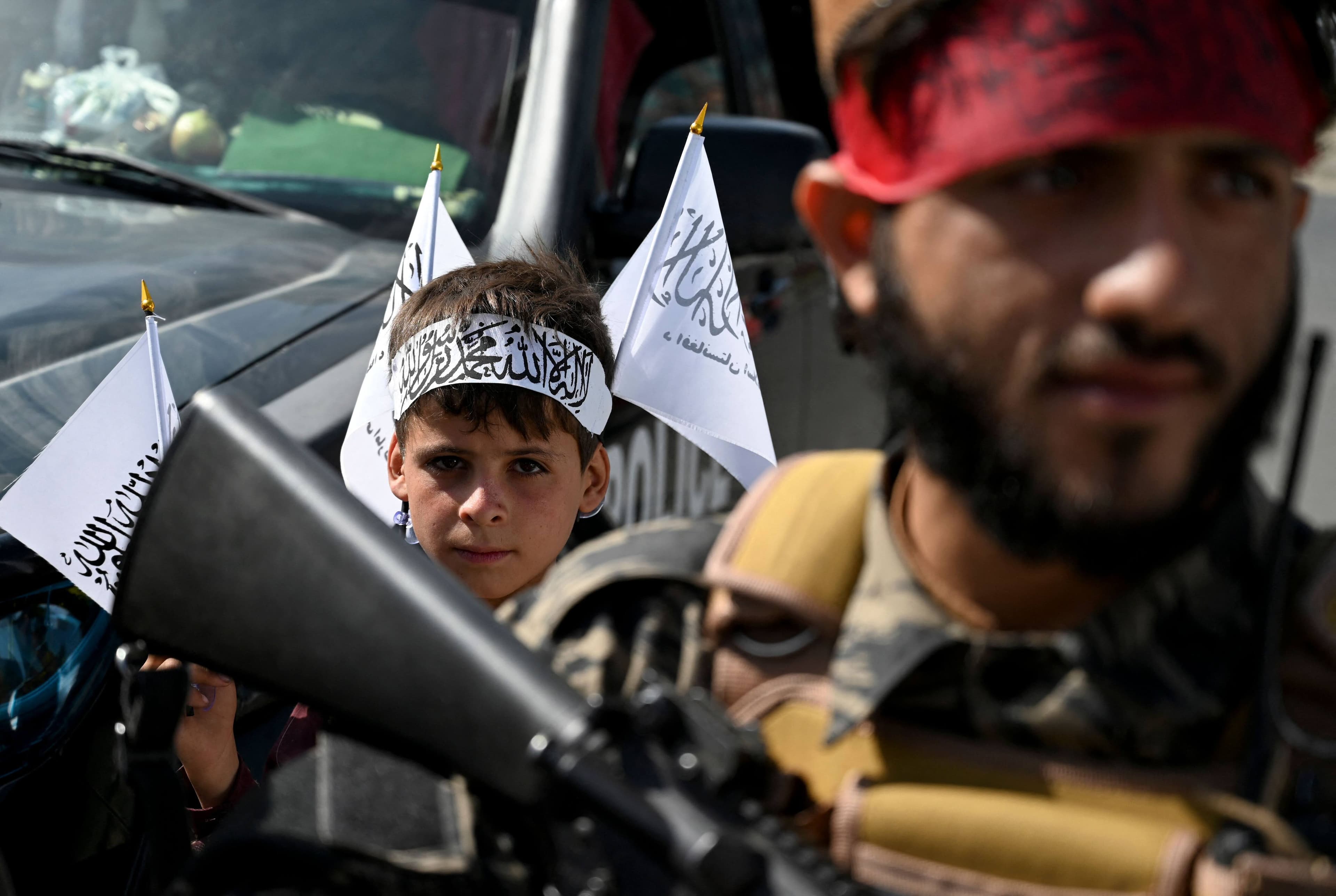 Un garçon, portant un bandeau et des drapeaux aux couleurs des talibans, accompagne un soldat qui monte la garde sur une route de Kaboul.
