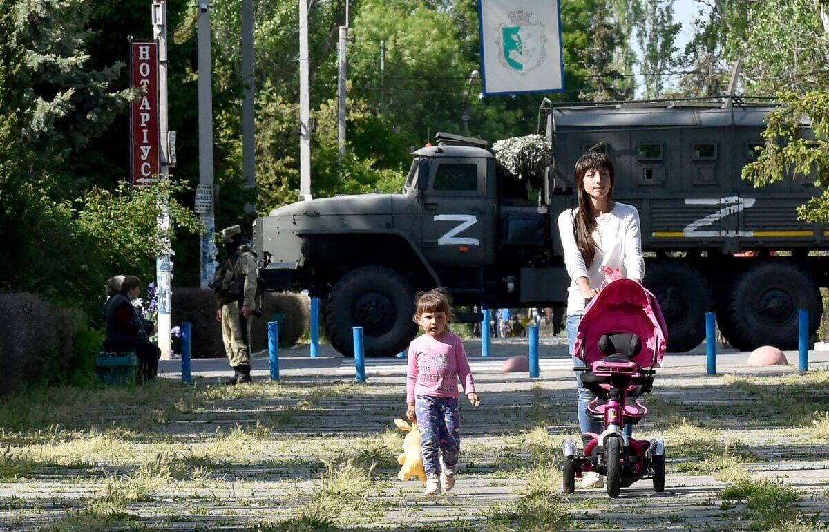 Une femme et son enfant marchent dans un parc devant un patrouilleur russe à Skadovsk, dans l'oblast de Kherson.