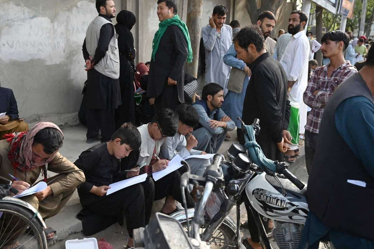 Les Afghans remplissent leurs coordonnées sur une feuille de papier pour enregistrer leur nom afin de quitter le pays devant l'ambassade britannique et canadienne à Kaboul le 19 août 2021 après la prise de contrôle militaire de l'Afghanistan par les talibans.