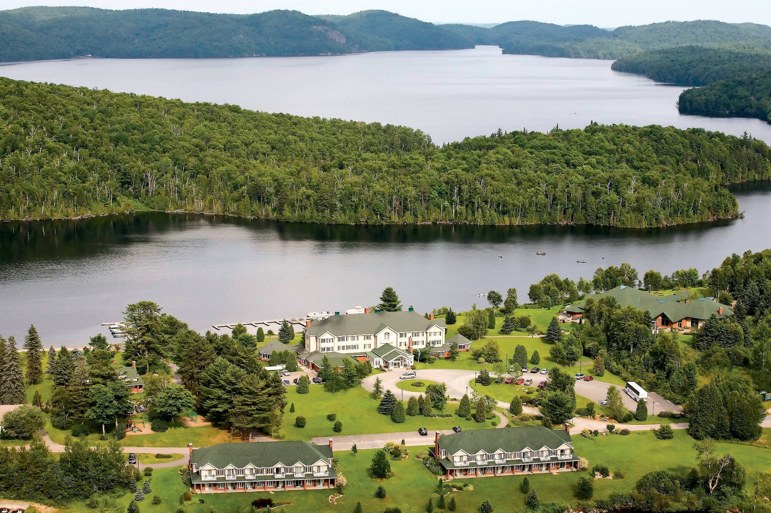 Le site enchanteur de l’auberge du Lac-à-l’Eau-Claire, avec deux pavillons, le centre aquatique à droite et la forêt autour.
