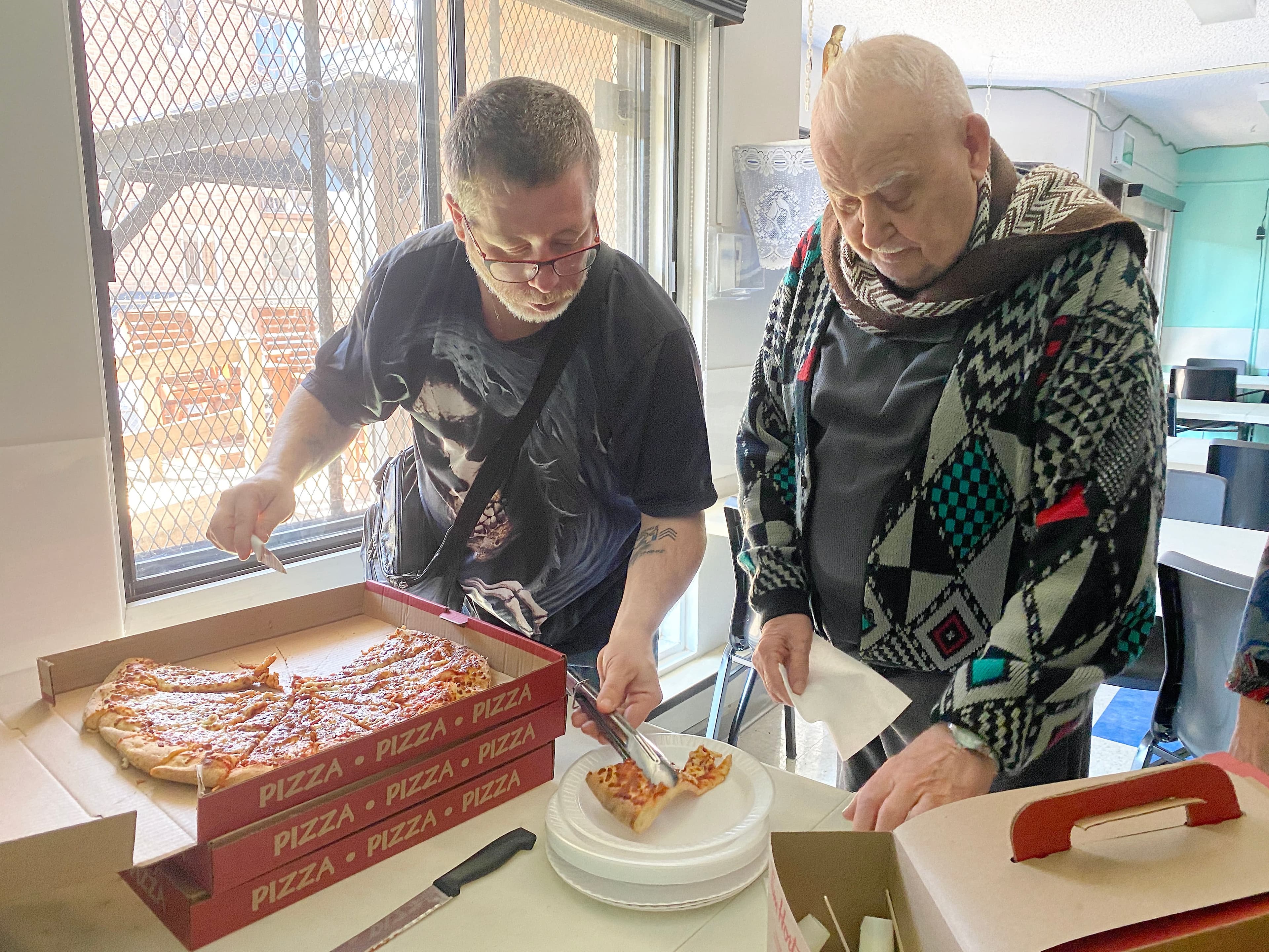 Le citoyen bon samaritain Claude Ducharme sert au résident Jean-Paul Ménard de la pizza apportée par des citoyens venant en aide au HLM.