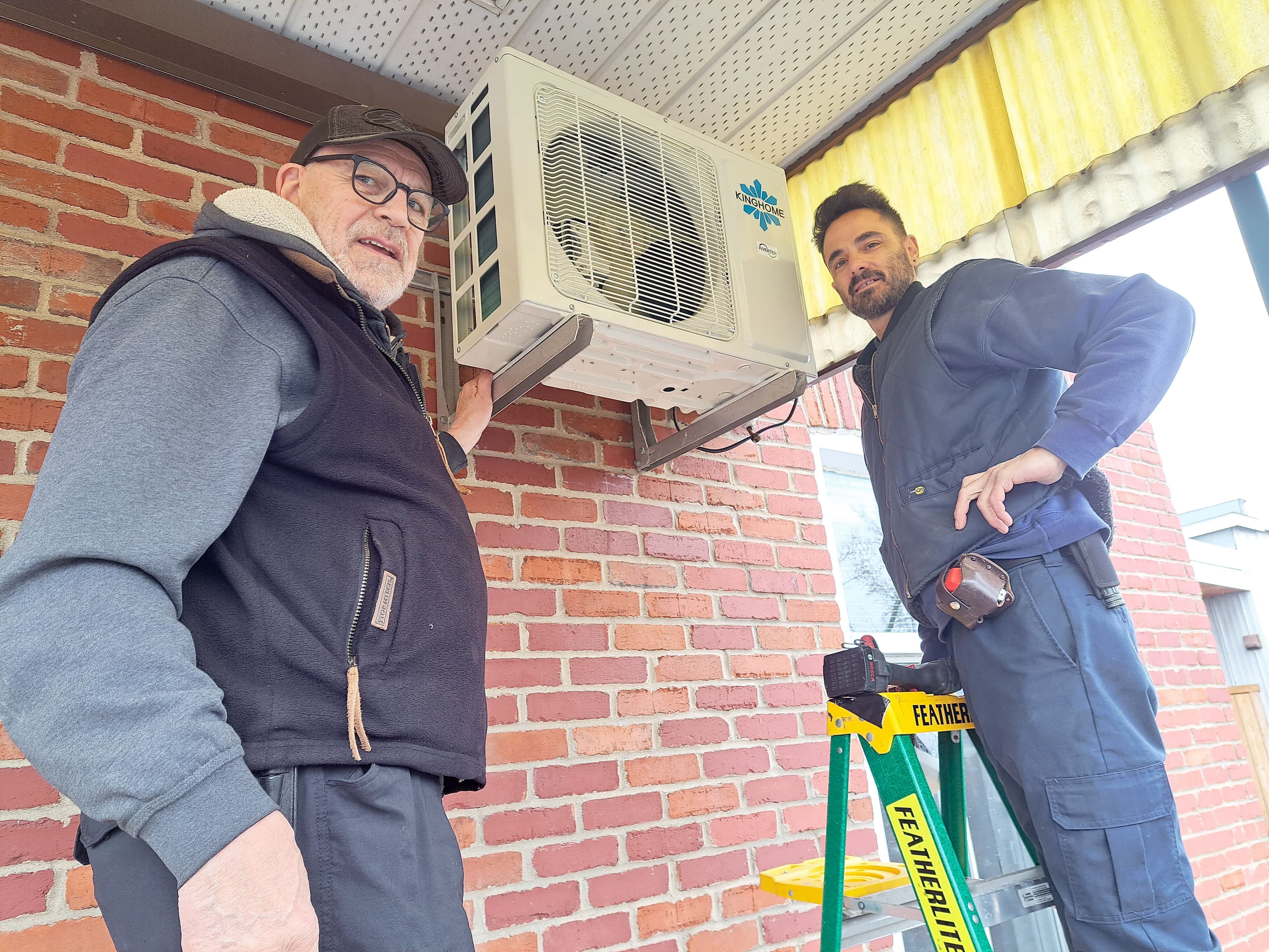 Patrick Bourassa et son collègue Jean Gosselin installent une thermopompe sur le balcon arrière d’un appartement du quartier Rosemont, à Montréal.
