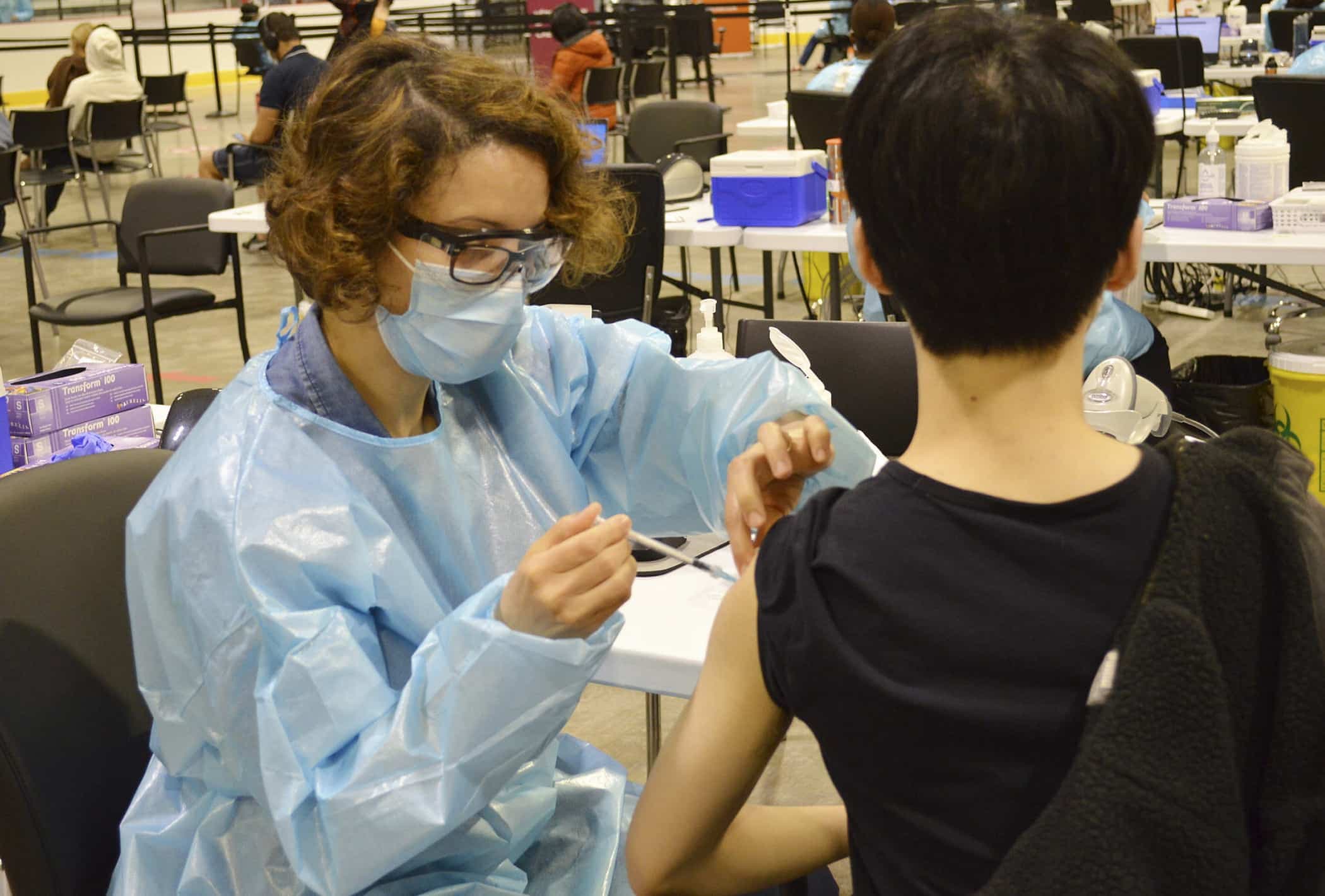 Hiba Saadi, vaccinatrice à l'aréna Bill-Durnan de Montréal, vaccine un jeune homme le 27 mai 2021.
