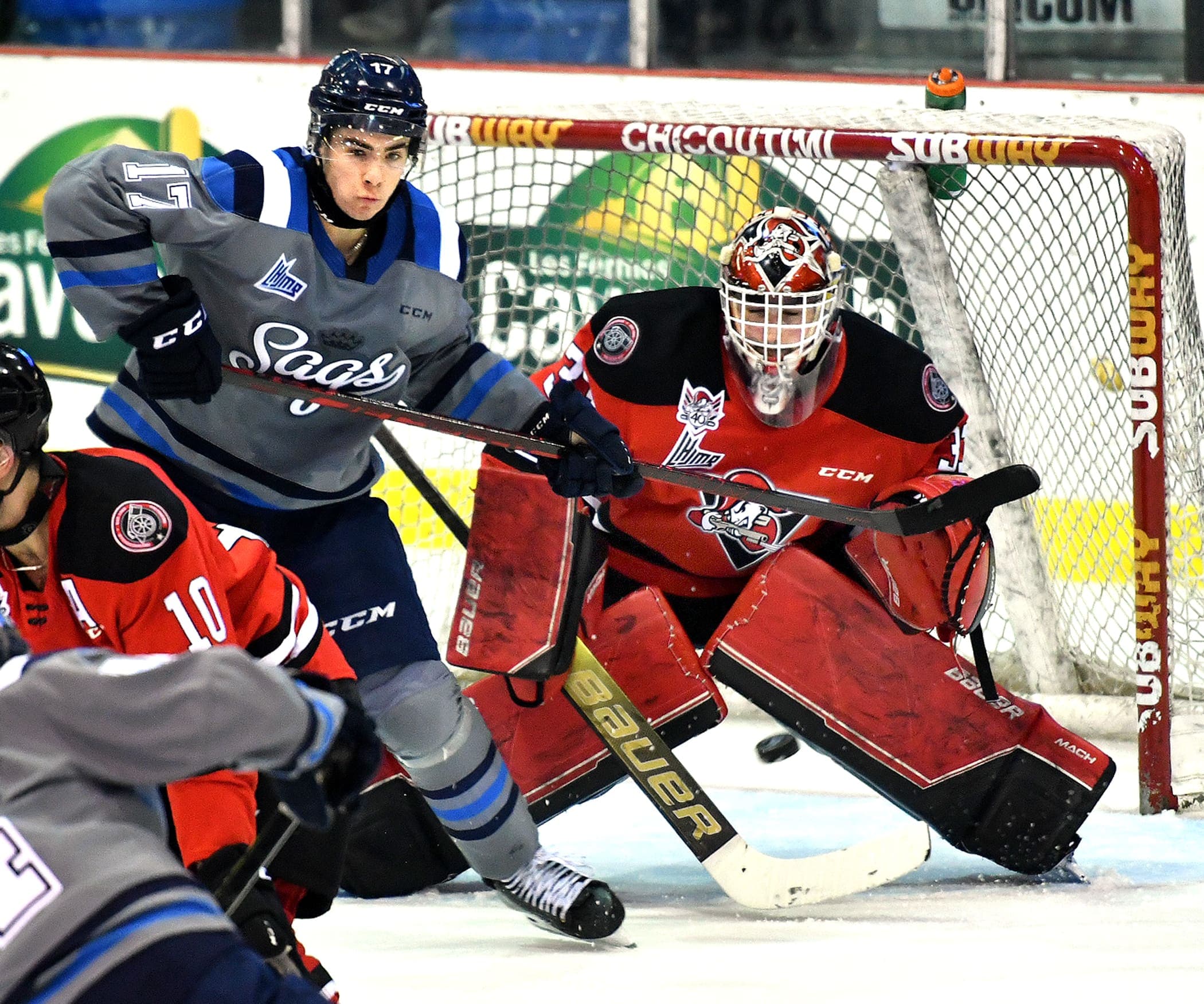 Le gardien des Voltigeurs, Jacob Goobie, tente d’effectuer un arrêt malgré le fait qu’il a la vue partiellement obstruée par Jakob Newcombe, des Saguenéens de Chicoutimi.