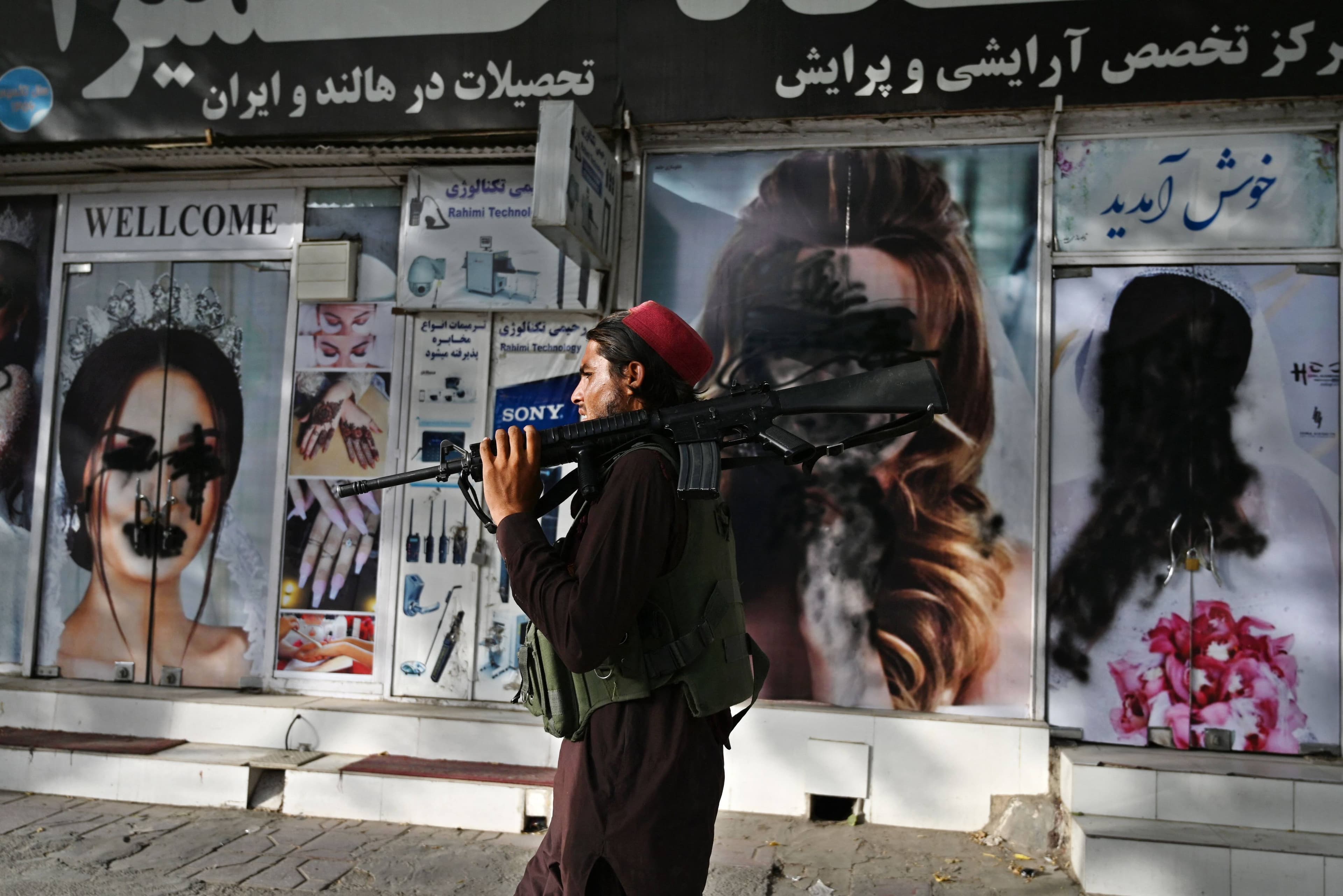 Un combattant taliban marche devant la devanture d'un salon de beauté vandalisé.