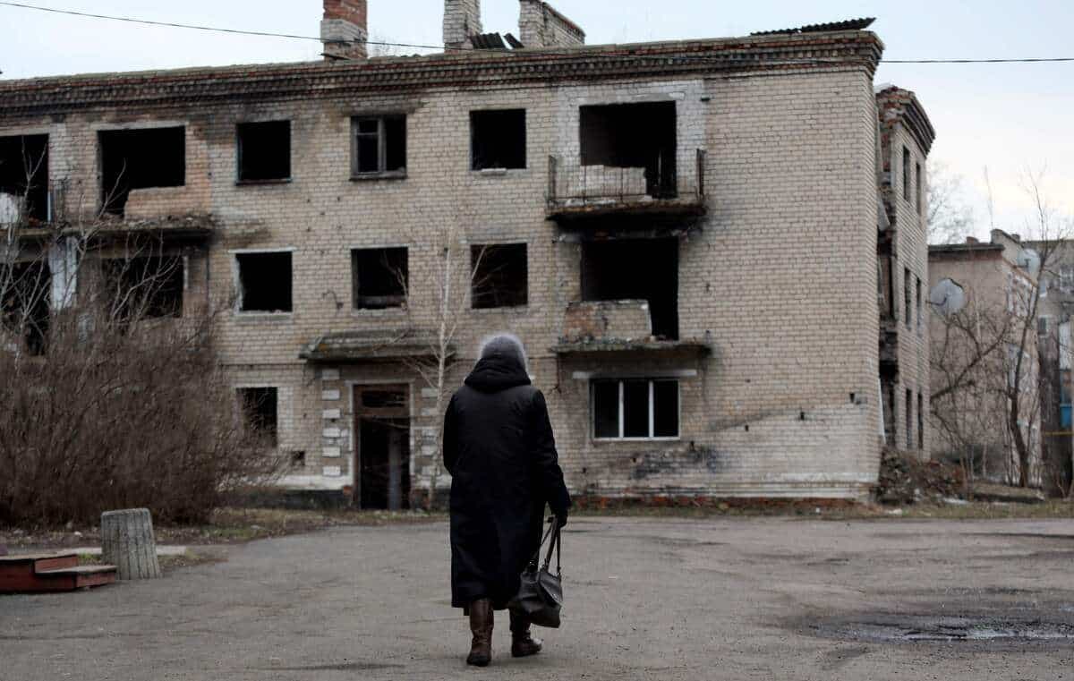 Une dame marchant devant immeuble détruit en Ukraine.
